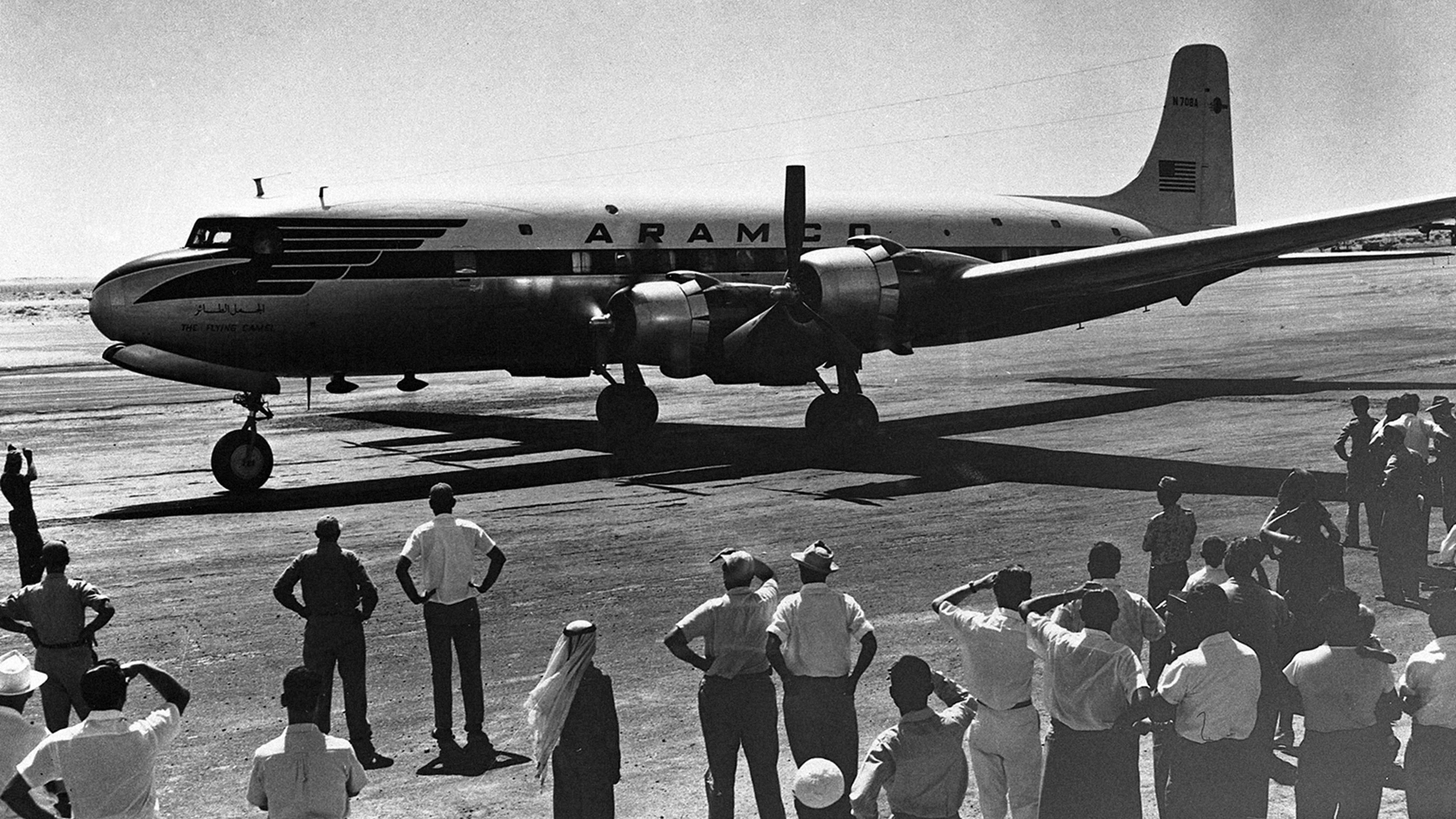 A group of people standing next to a Saudi Aramco (Mukamalah) plane at a landing strip