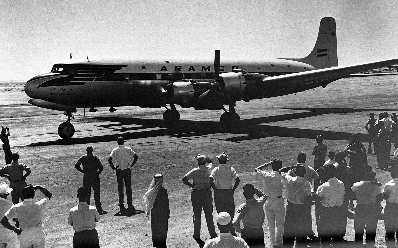 A group of people standing next to a Saudi Aramco (Mukamalah) plane at a landing strip