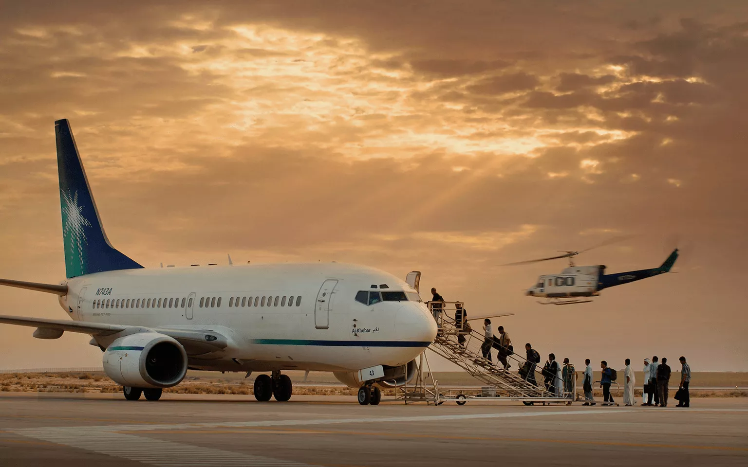 Mukamalah (Saudi Aramco) airplane waiting on a group of people to enter through the airplane stairs with a background of a golden sunset